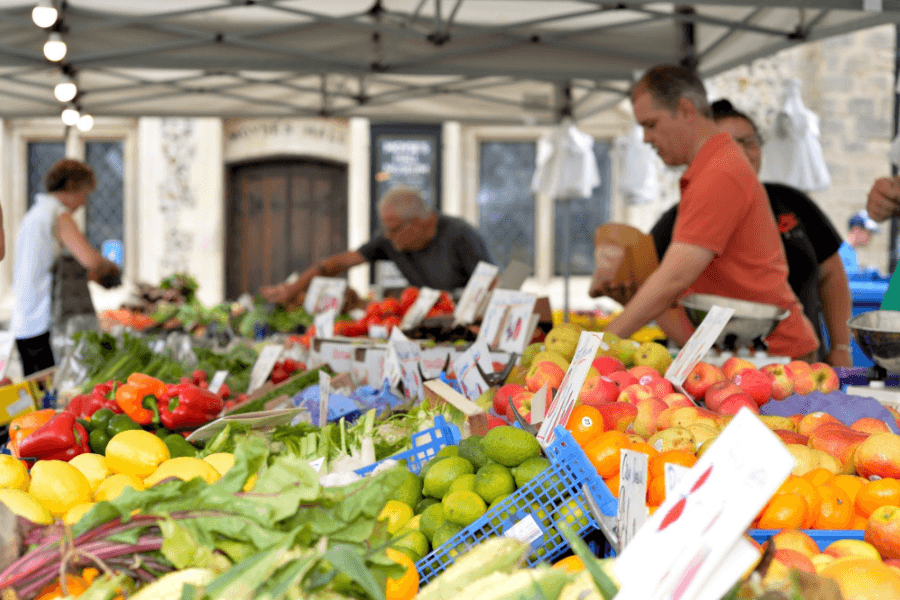 A fruit vendor stand in front of their fresh produce, chatting with local Oshawa residents. Image courtesy of Danplowman.com.