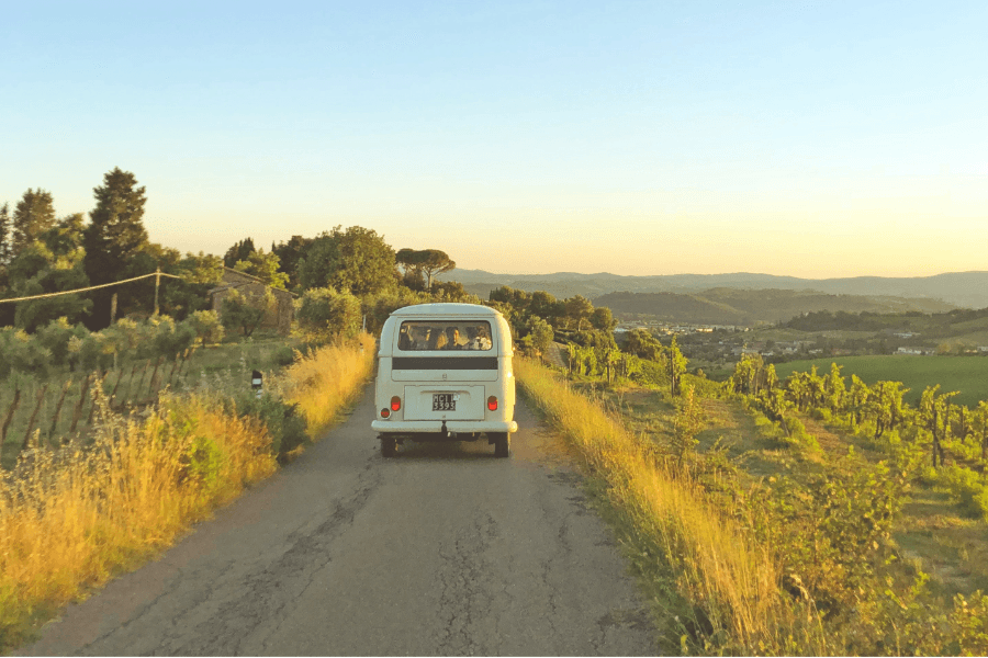 A van plods down the road into the sunset as rolling hills stretch away in the distance. Image courtesy of Unsplash.